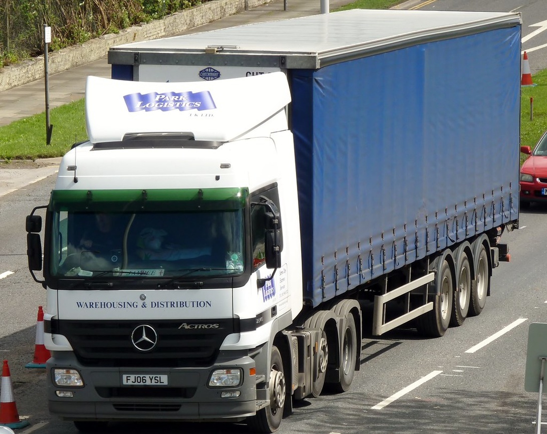 Ein weiß-blauer Mercedes Actros Sattelzug mit der Aufschrift 'WAREHOUSING & DISTRIBUTION' und dem 'Park Logistics' Branding, der traditionelle Logistikoperationen repräsentiert.