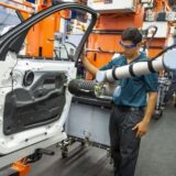 Mitarbeiter arbeitet neben einem kollaborativen Roboter an einer Autotür