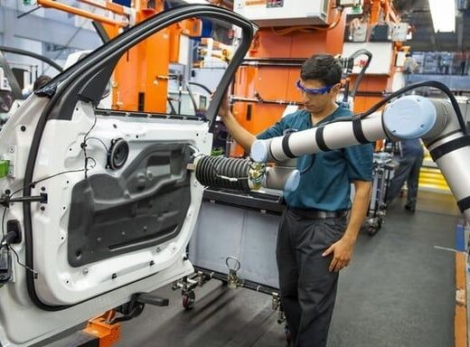 Mitarbeiter arbeitet neben einem kollaborativen Roboter an einer Autotür