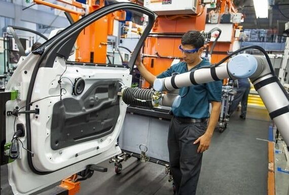 Mitarbeiter arbeitet neben einem kollaborativen Roboter an einer Autotür